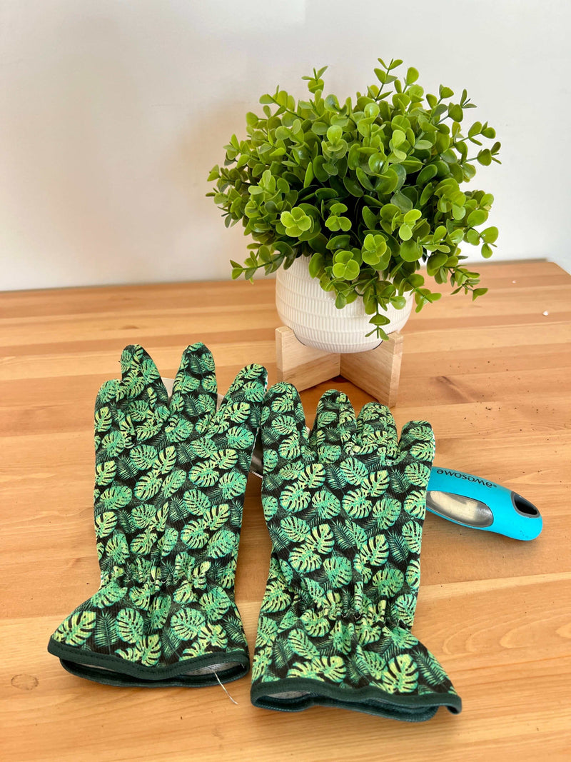 Pair of stylish Fancy Gardening Gloves with green leaf pattern on wooden table next to potted plant and gardening tool